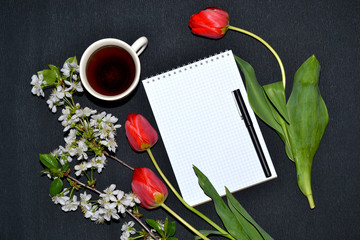 Note pad, pen, white flowers and tulips on dark surface.