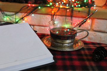 A Cup of coffee and a clean diary on the background of a burning fireplace and Christmas lights