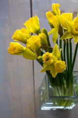 Bouquet of yellow narcissus in the glass on the wooden background