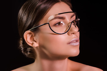 portrait of beautiful woman in fashionable eyeglasses with bare shoulders looking away isolated on black