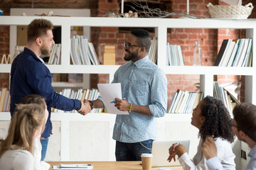 Smiling African American employer handshake millennial worker greeting with good work result during...