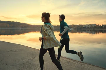Papier Peint photo autocollant Jogging Young man and woman out for a run on the lake at the sunrise