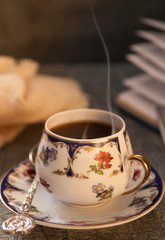 Hot coffee in a cup with floral decoration. Diary with plans and pen. On a dark background. Blurred