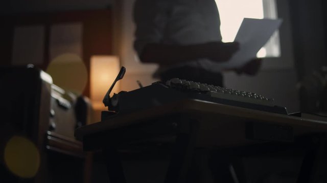 Young man walks around his office and sits down to write at a dusty vintage typewriter
