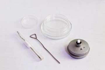 . A set of tools for bacteriological research. A metal loop, a sterile test tube, closed with a cotton swab, a spirit lamp, Petri dishes on a white gauze background.