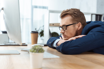 focused businessman in eyeglasses sitting at table with computer monitor in office