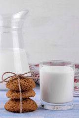 oatmeal cookies piled in the stack in the foreground and milk in a glass on a blue wooden table. bake. yummy.
