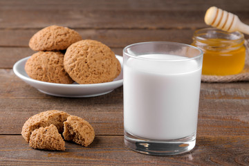 Tasty oatmeal cookies with honey and milk on a napkin on a brown wooden table