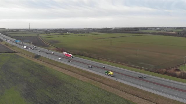 Aerial 4k footage of a Motorway highway in the UK, showing cars, vans, and trucks traveling on the road.