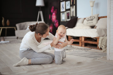 Mother comforts crying baby on floor in room.