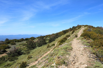 A landscape of a path on the edge of Peña Oroel mount, with the Pyrenees as background, a wide valley with blue sky and some bushes, in Aragon, Spain