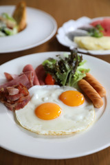 Breakfast set with fried eggs, bacon, sausages, beans, toasts, fresh salad and fruit on wood table