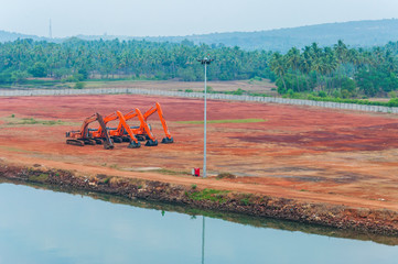 Orange excavators on a construction site beside the river bank