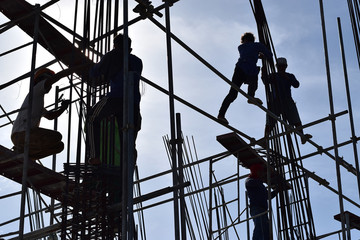 Filipino Construction steel workers assembling steel bars on high-rise building with no proper protective suits and safety shoes. underside view, silhouettes