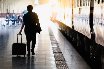 Back view of man traveler walking with suitcase in railway station with sun light blured background...