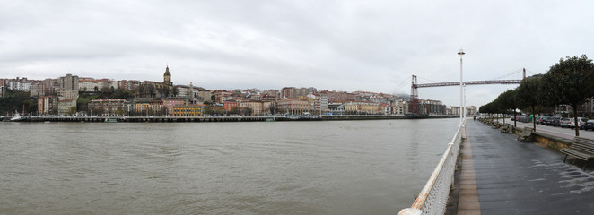 A sight of Portugalete from the river promenade, with the aerial Vizcaya bridge (Puente de Vizcaya) on Nervion river in a cloudy winter day, Spain