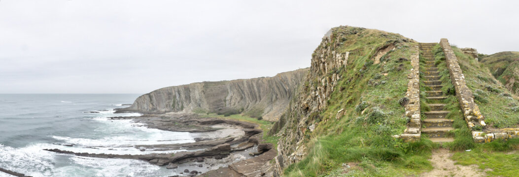 Landscape of staircase on the high cliffs on a rough sea during a cloudy rainy day from Paseo de la Galea in Getxo town, in the Basque Country, Spain