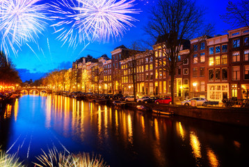 Obraz premium Houses over canal with lights and reflections at night with fireworks, Amsterdam, Netherlands,