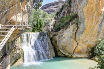 An idyllic waterfall in the Vero river canyon, with light blue water and mountains on the background during a summer day in Alquezar, Spain