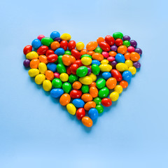 Colorful candies arranged as heart on blue background