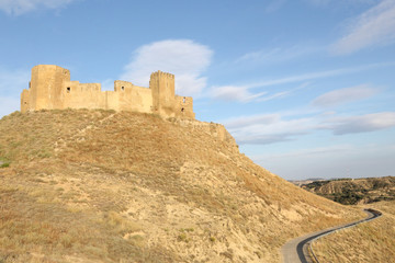 A landscape of the medieval abandoned Montearagon castle, placed over a hill among tilled crop fields, in a summer afternoon, in Aragon region, Spain