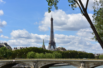 Paris, France. Bridge and Eiffel Tower from Seine river walk. Trees, branches and blue sky with clouds. 