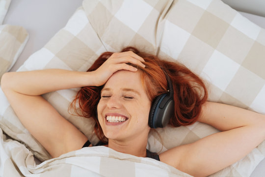 Young woman lying in bed listening to music