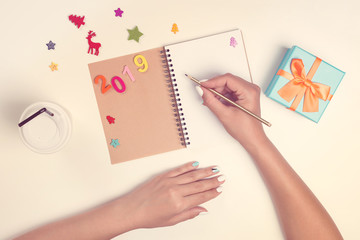 2019 goals list with notebook on white desk. Female hands are writing on notebook.Christmas planning concept . To do list. Mockup, copy space.