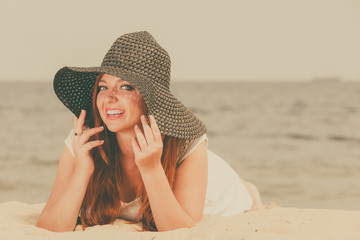 Redhead woman wearing sun hat lying on beach