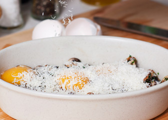 Baking dish with mushrooms, raw eggs and grated Parmesan