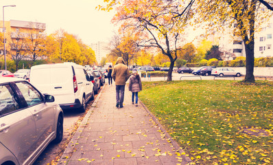 Father with little daughter walking outside in autumn outfit from back.