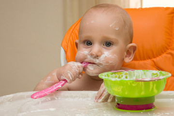 A baby boy in a orange high chair eating yoghurt