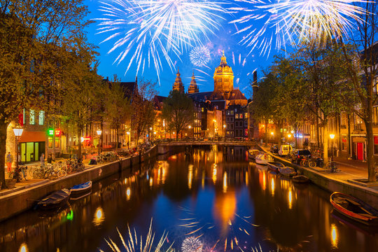 Church of St Nicholas and red lights quater over old town canal at night with fireworks, Amsterdam, Holland