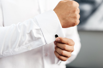 Handsome man, groom buttoning black cufflink on white shirt