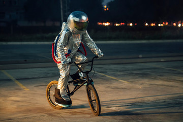 Spaceman in the city at night on parking lot riding BMX bike