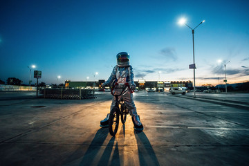 Spaceman in the city at night on parking lot with BMX bike
