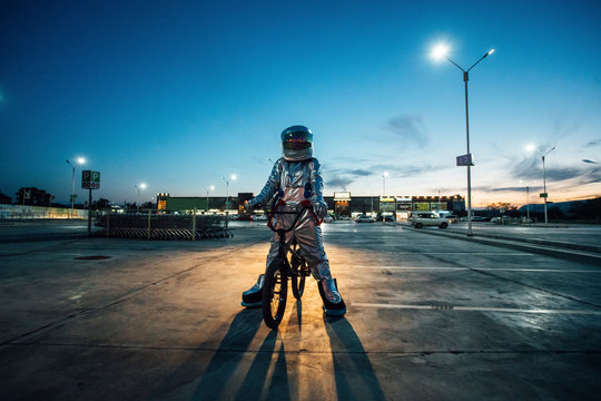 Spaceman in the city at night on parking lot with BMX bike