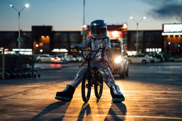 Spaceman in the city at night on parking lot with BMX bike