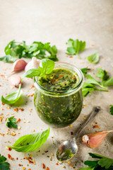 Argentinian traditional food, raw homemade green Chimichurri salsa or sauce woth parsley, garlic, basil leaves, hot pepper and spices, light stone table copy space