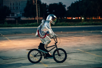 Spaceman in the city at night on parking lot riding BMX bike