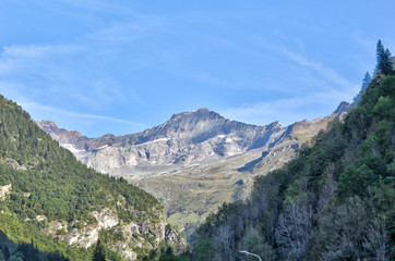 A landscape of blue cloudy sky, high mountains, fir and pine tree forests and green pastures in Val d'Otro, Piedmont region, Alps mountains, Italy