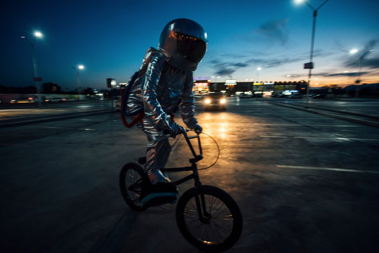 Spaceman in the city at night on parking lot riding BMX bike - Powered by Adobe