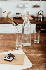 close up view of remote car key, bottle of water and branch in vase at wooden table in kitchen