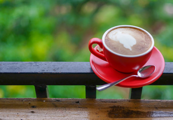 Red cup of coffee on black steel balcony rail with blur background