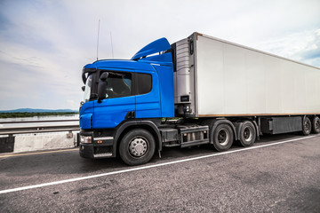 Fototapeta premium Blue truck on a road with refrigerator trailer