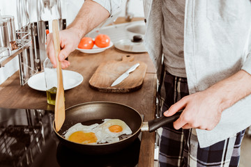 cropped image of young man cooking eggs on frying pan in kitchen