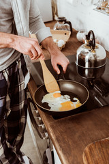 cropped image of man cooking scrambled eggs on frying pan in kitchen