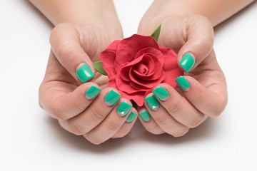 green, mint moon manicure with crystals on short square hands with a red rose in the palms on a white background close-up
