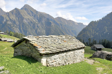 A stone hut in the Walser town of Follu, among high mountains, pine forests and green pastures, in summer, in Val d'Otro valley, Alps mountains, Italy