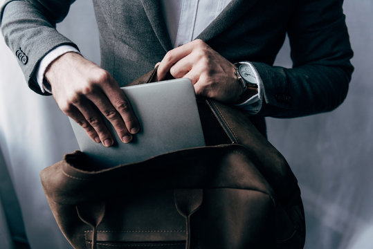 cropped image of businessman in jacket putting laptop in bag